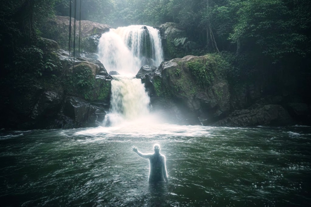 Ethereal figure in water near Perunthenaruvi waterfall, mist-shrouded forest backdrop