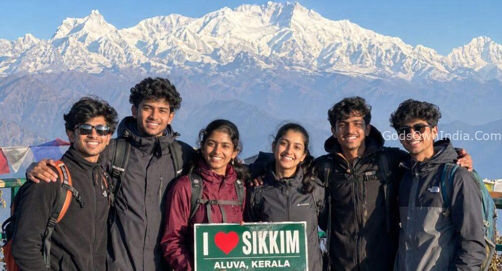 A group of young Indian travelers (age 18-20, appearing to be from Aluva, Kerala) standing at a viewpoint in Sikkim