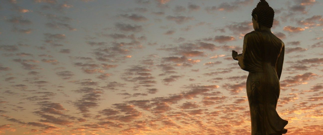 a statue of a person standing in front of a sunset