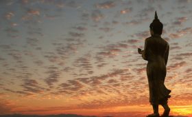a statue of a person standing in front of a sunset