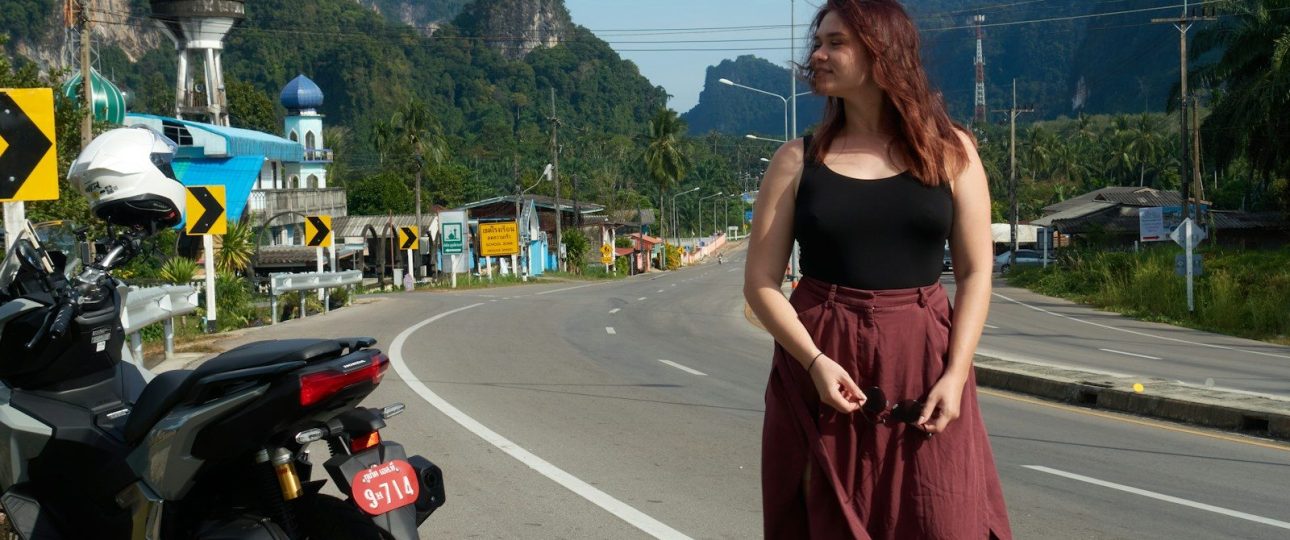 Woman walking on road with motorcycle and mountains.