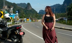 Woman walking on road with motorcycle and mountains.